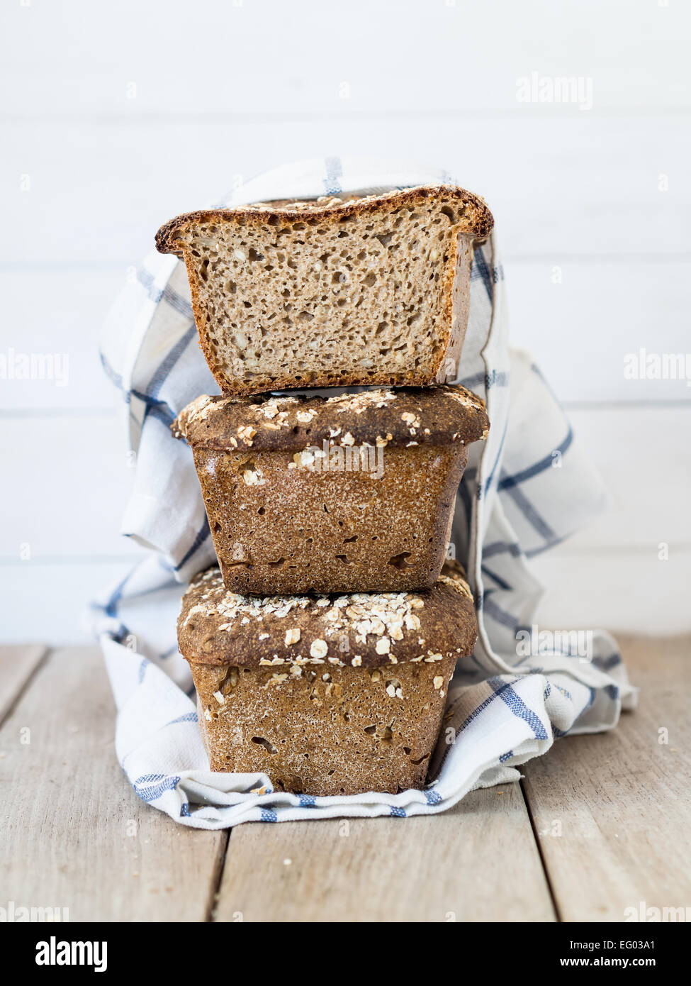 Vertical photo of a pile of three homemade whole grain mixed rye-wheat sourdough breads with seeds on a clear wooden background. Stock Photo