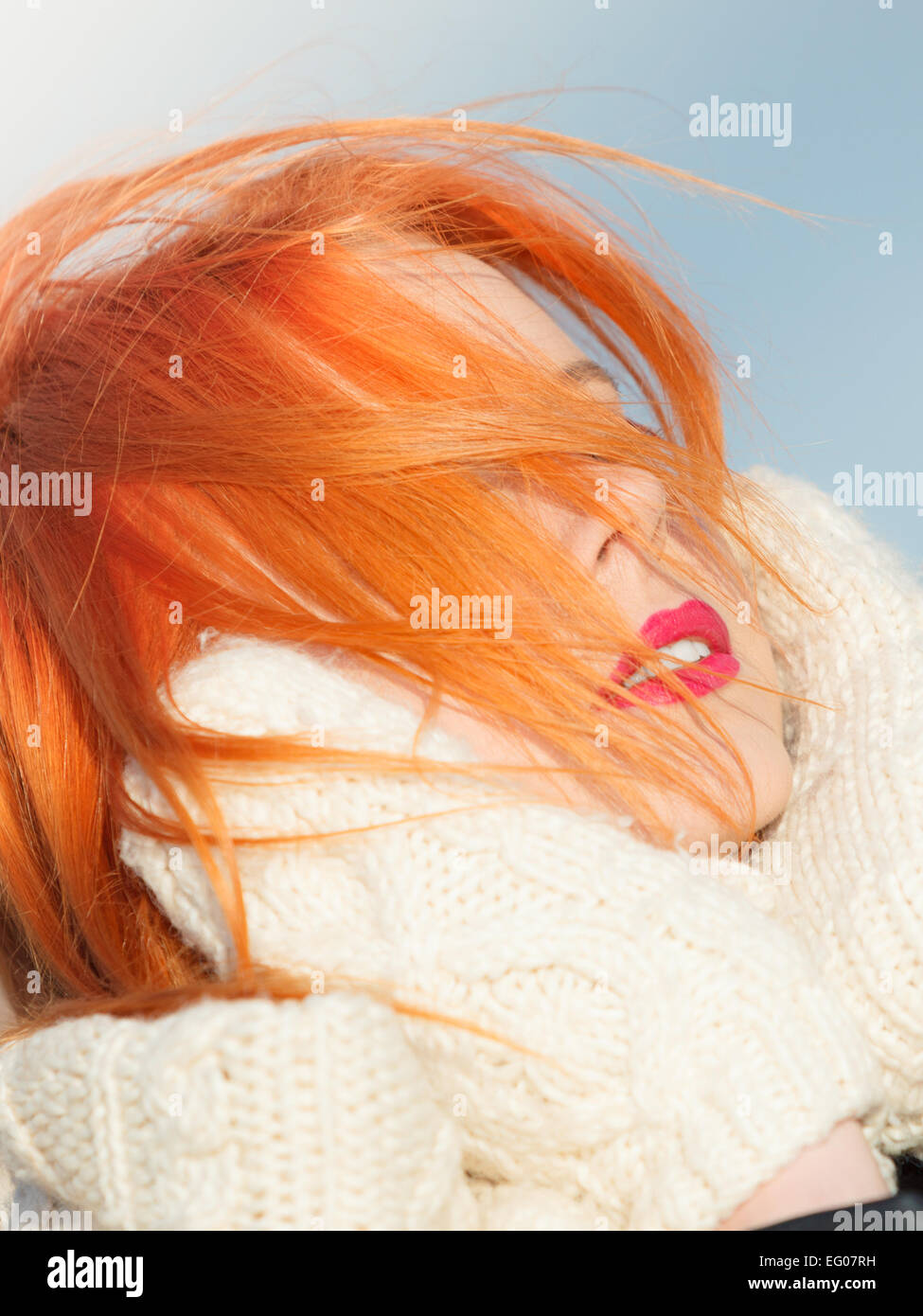 Winter fashion. Beauty redhaired head with hair blowing on wind, woman in warm clothing outdoor enjoying sunlight. Stock Photo