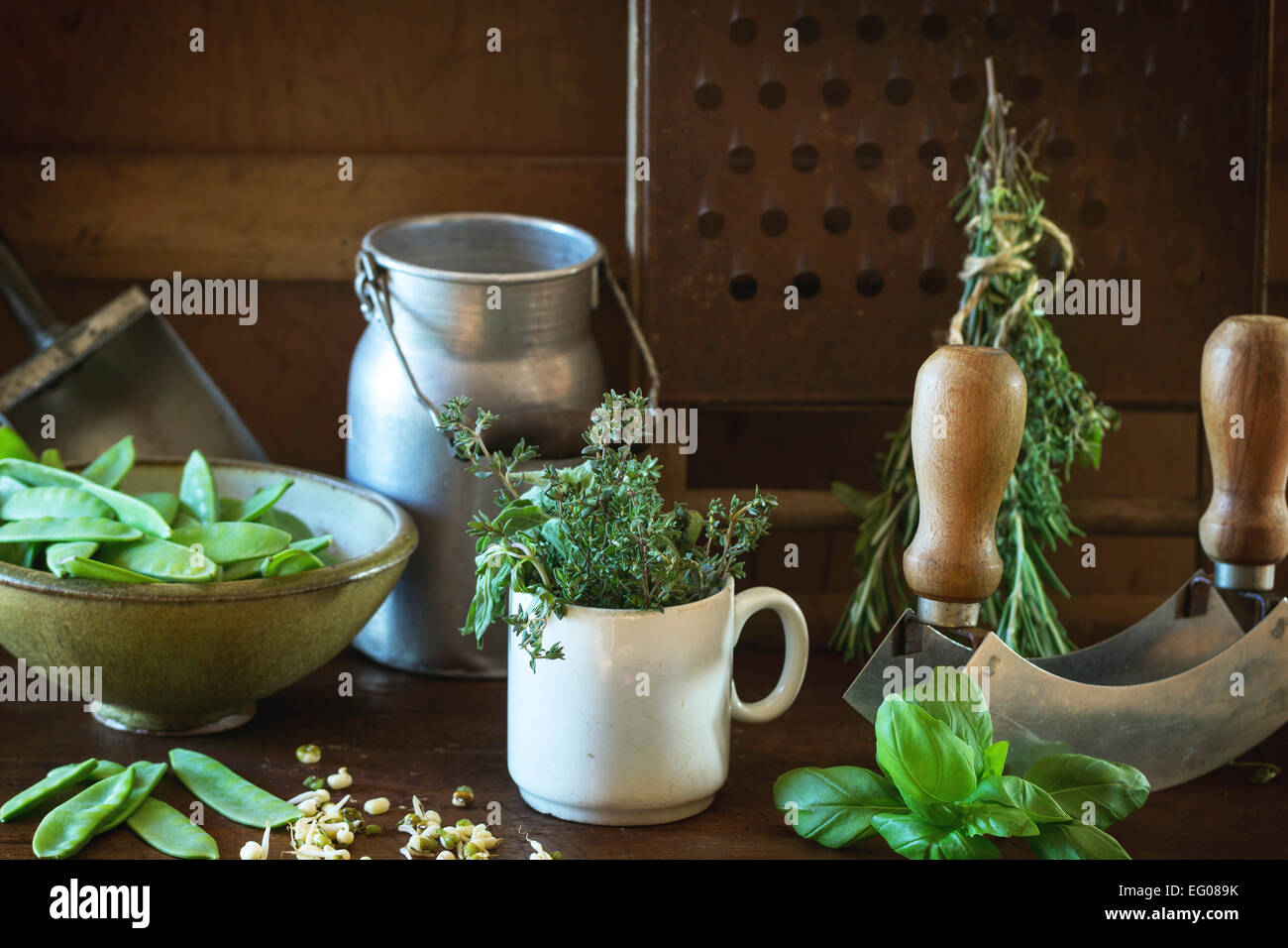 Young sweet peas and mix of herbs rosemary and basil with vintage kitchen utensil over wooden table Stock Photo