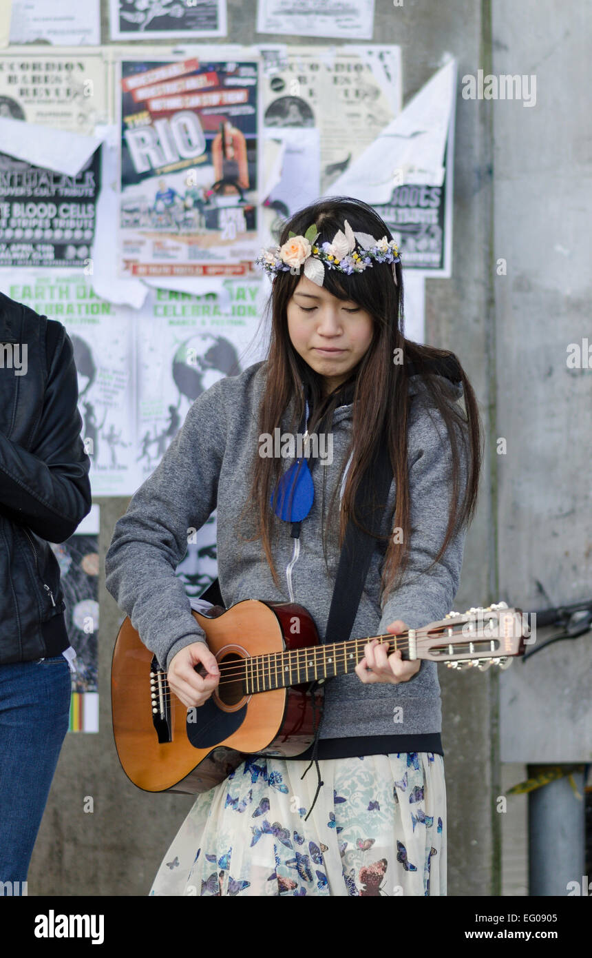 Young hippie girl with flowers in her hair playing guitar on the street. Stock Photo