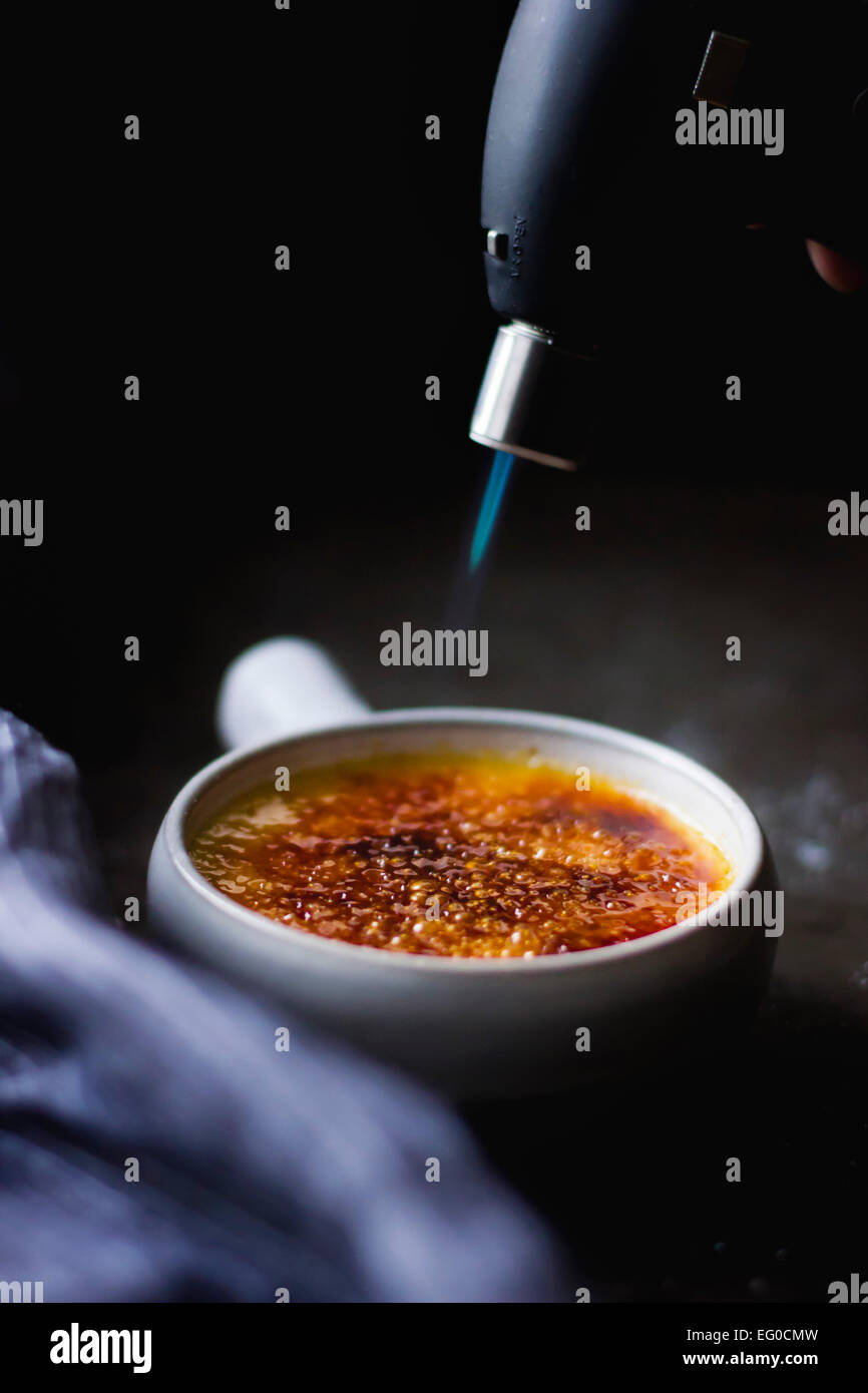 Melting sugar on a creme brulee dessert with a blow torch Stock Photo