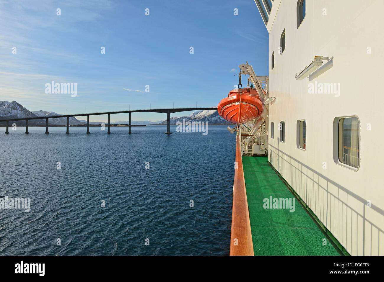 Orange lifeboat and railing of the Kong Harald in the blue Risøysound with bridge, 26 February 2014 Stock Photo