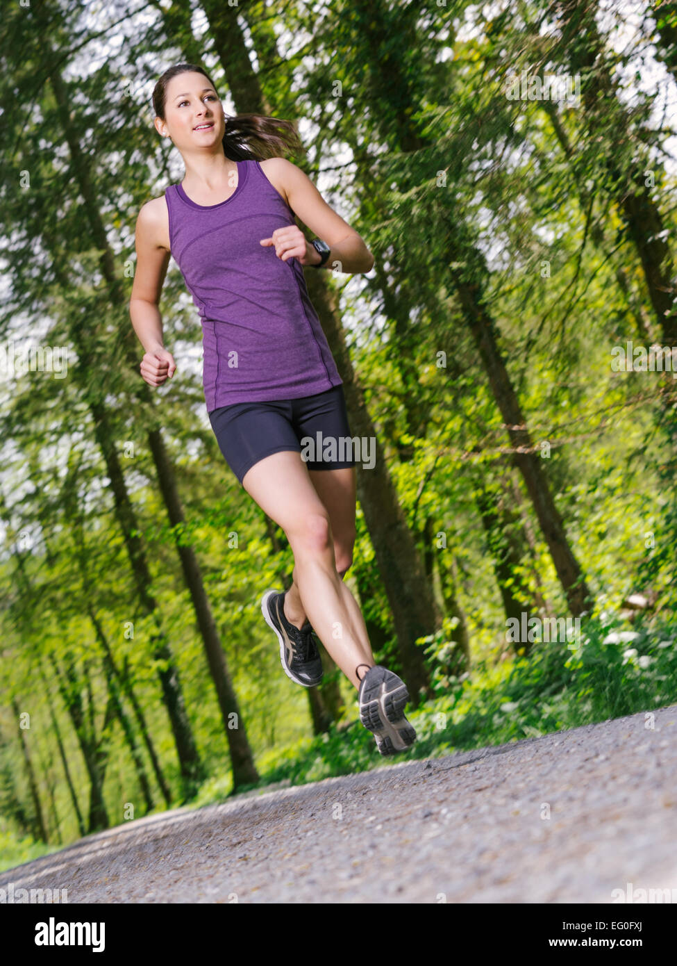 Photo of a young woman jogging and exercising on a gravel path through a forest. Slight motion