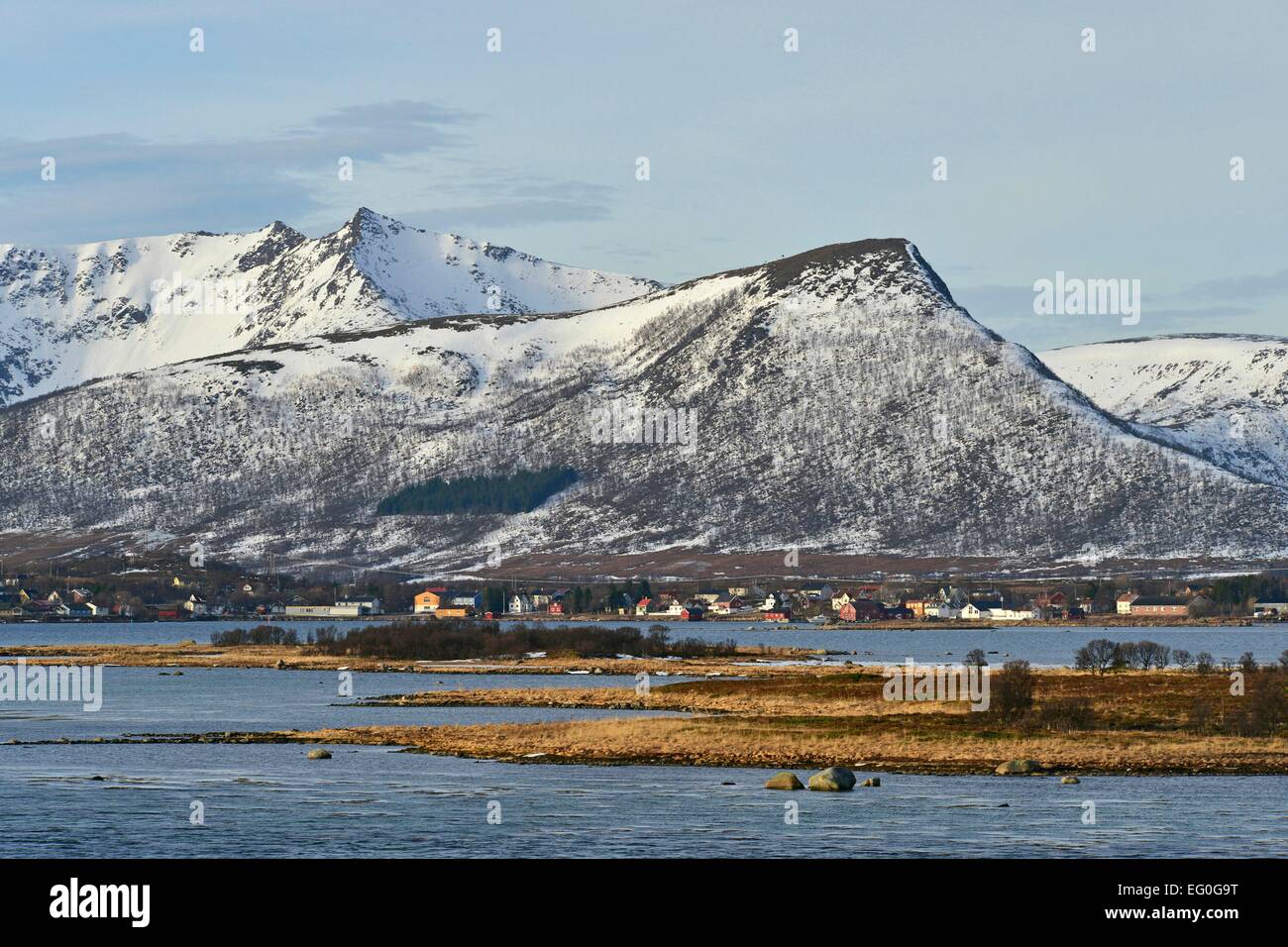 Flat islands in front of the houses of Risøyhamn, the buildings stand in the shadow of mighty mountains; 26 February 2014 Stock Photo