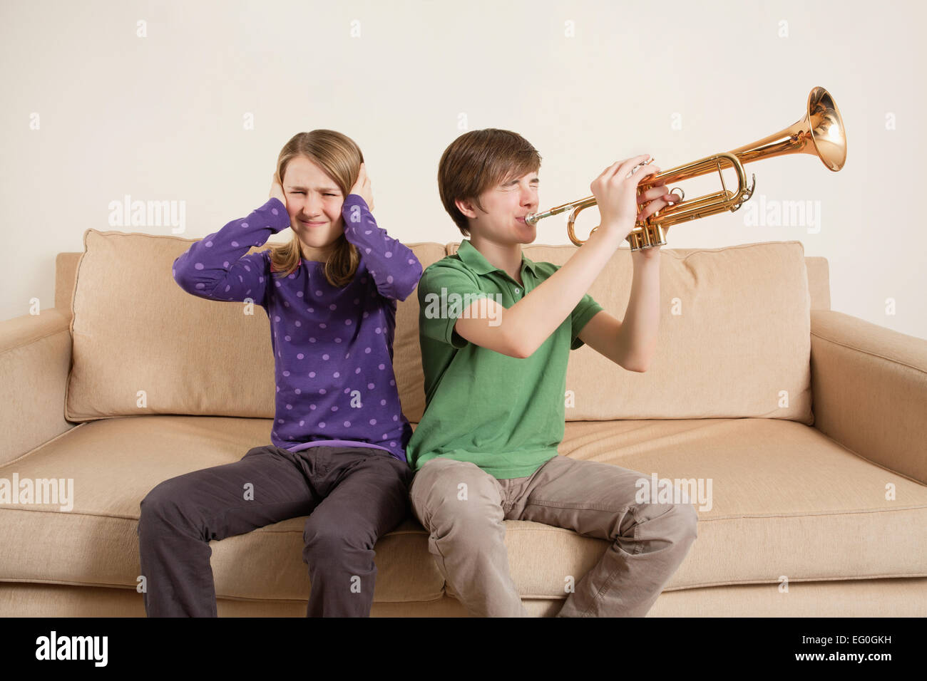 Photo of a brother playing his trumpet too loudly, or badly, and annoying his sister. Stock Photo