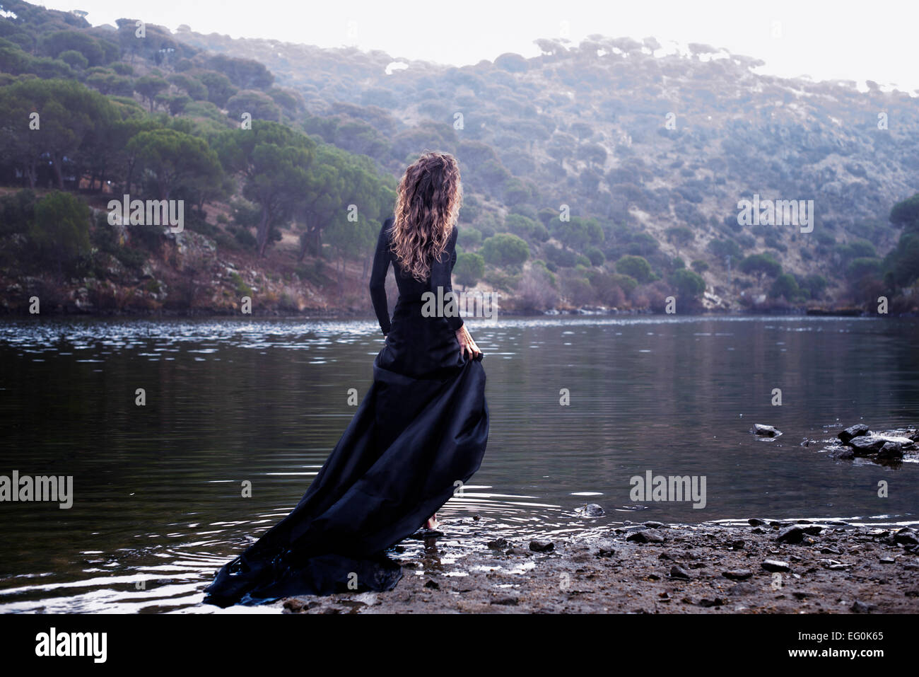 Woman in a long black dress walking into a lake Stock Photo - Alamy