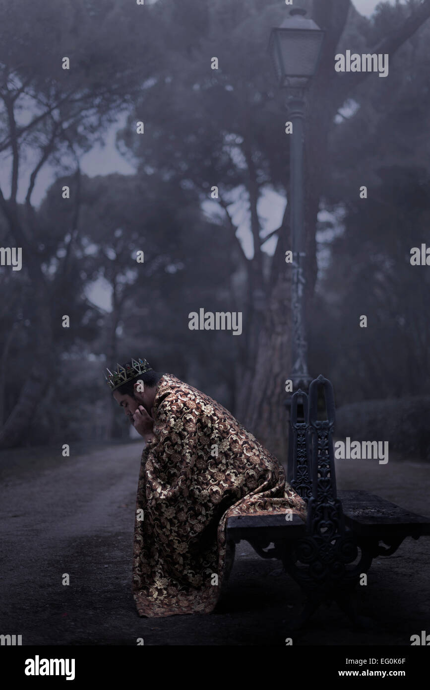 Man dressed in a king's robe sitting on a bench in a park Stock Photo