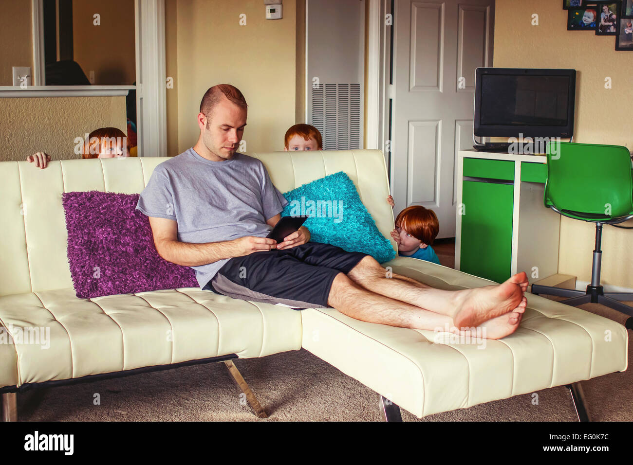 Three young boys hiding behind couch ready to surprise their father Stock Photo