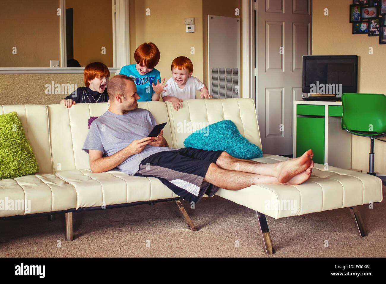 Three boys jumping out from behind a couch to surprise their father Stock Photo