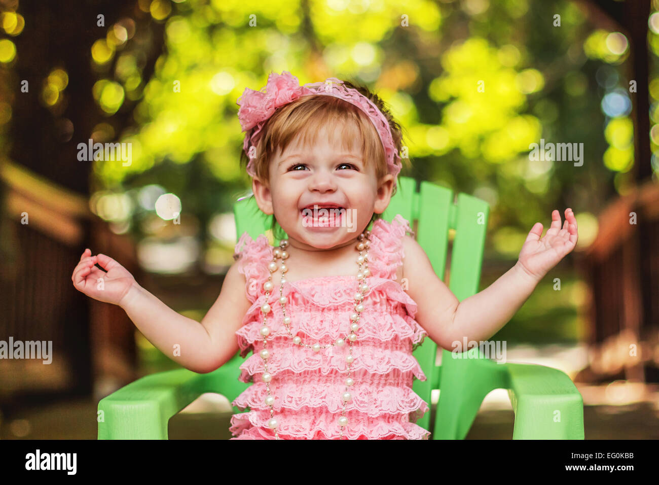 Happy girl in a party dress sitting in garden chair laughing Stock Photo