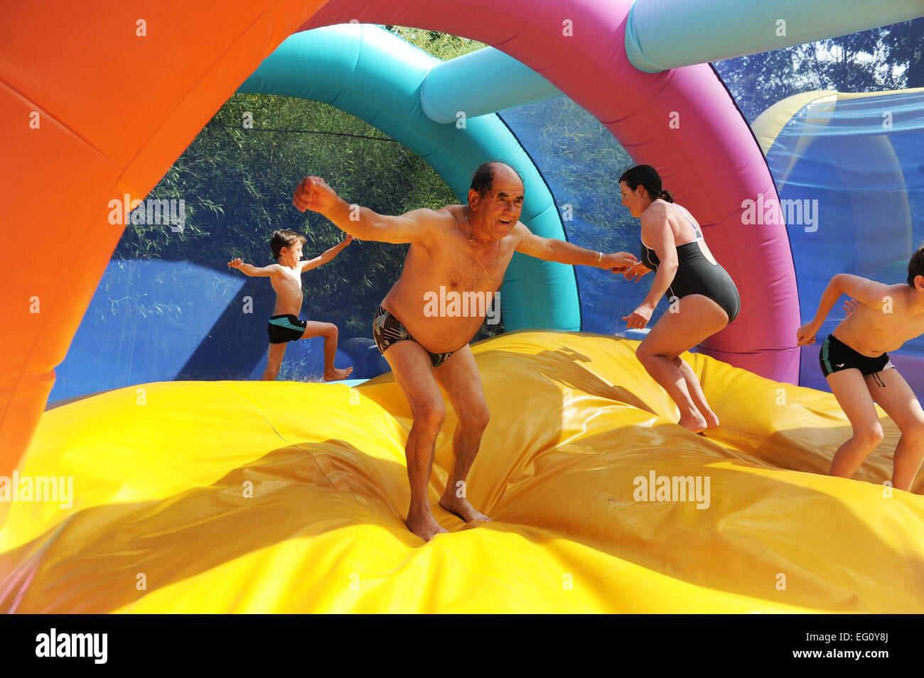 Three generations leaping together on a bouncy castle in Betaille Aquapark in France Stock Photo