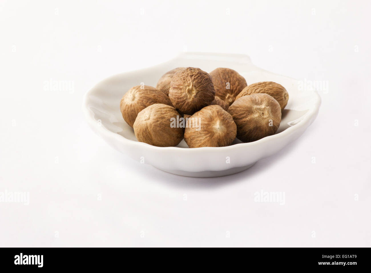 Nutmegs in white bowl on white background Stock Photo