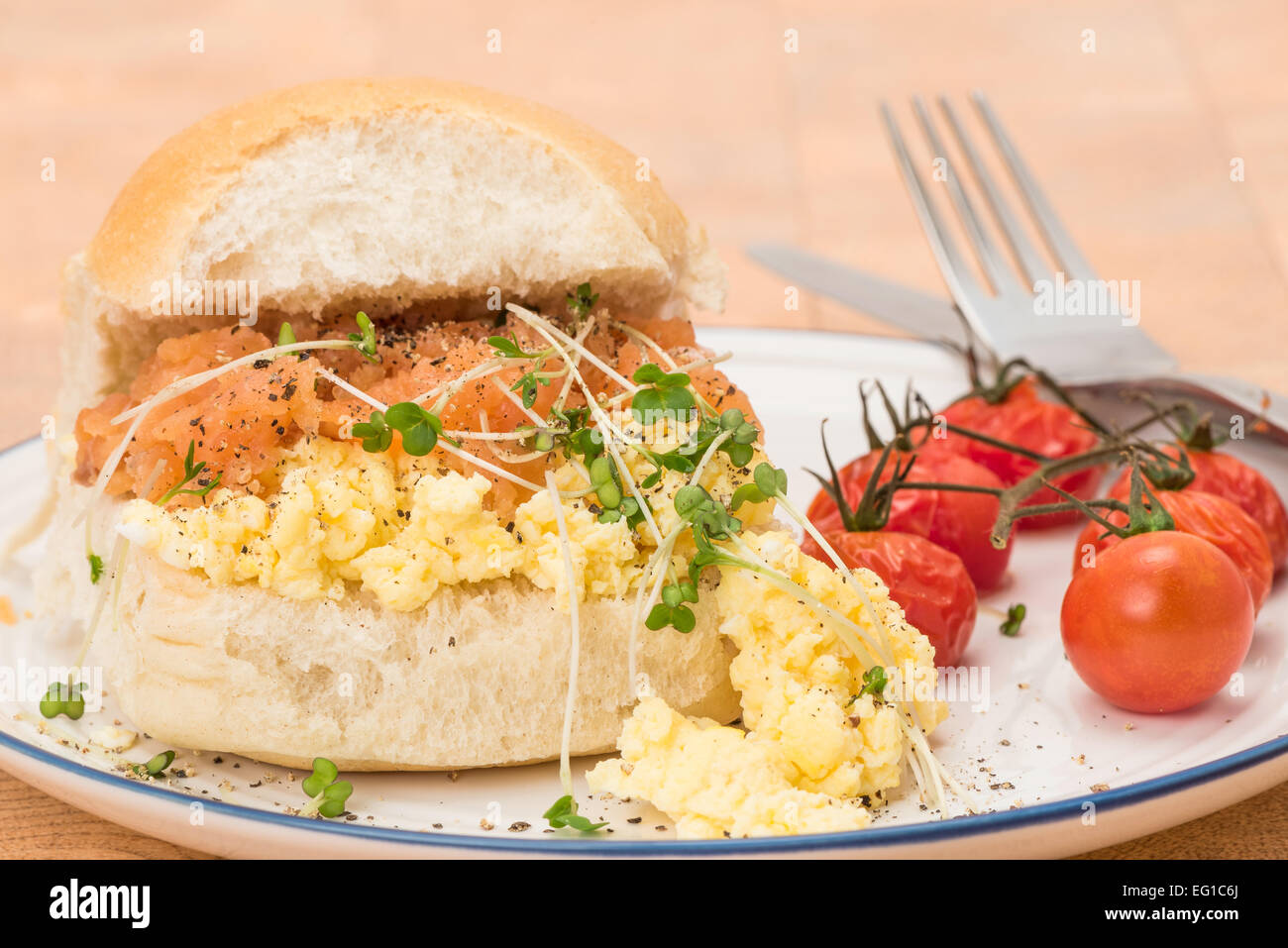 A smoked salmon and scrambled egg bread roll breakfast served with some grilled vine tomatoes - shallow depth of field Stock Photo