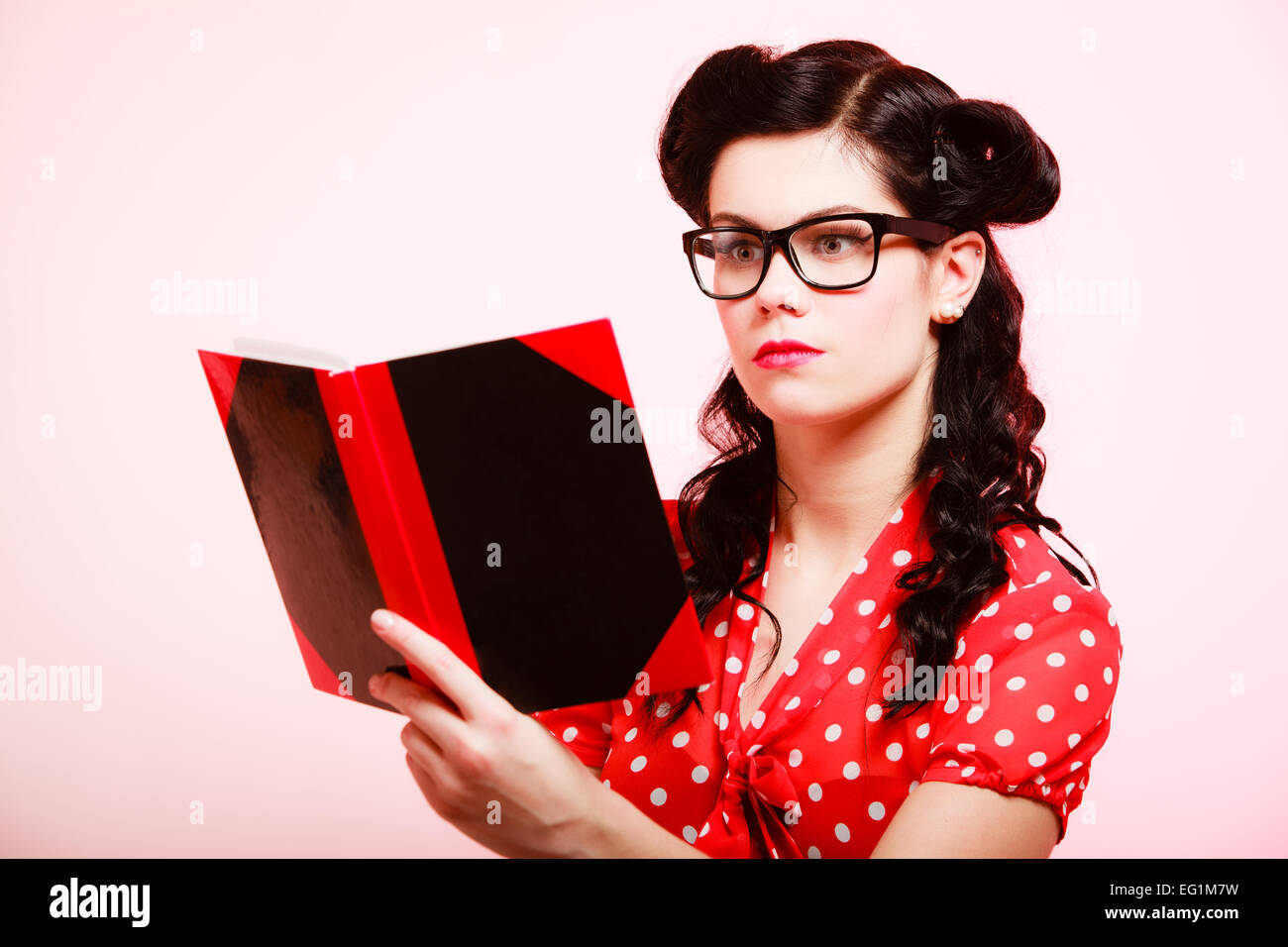 Retro. Stylish woman student or teacher in eyeglasses reading book on pink. Brunette girl in pinup style. Education. Stock Photo
