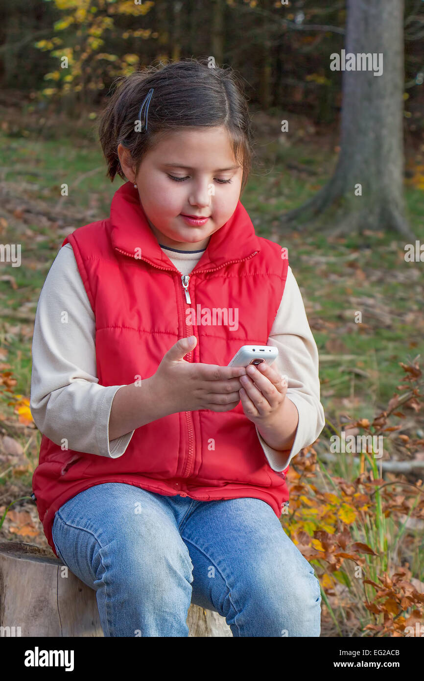 Cute kid, a girl, playing with a smart phone in forest. Illustrative of influence of technology on kids and our lives. Stock Photo