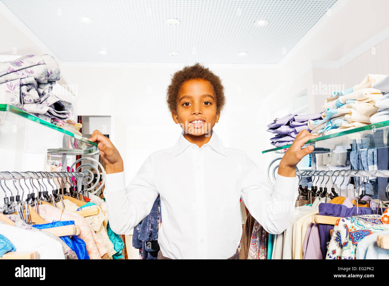 African boy in white shirt stand between hangers Stock Photo