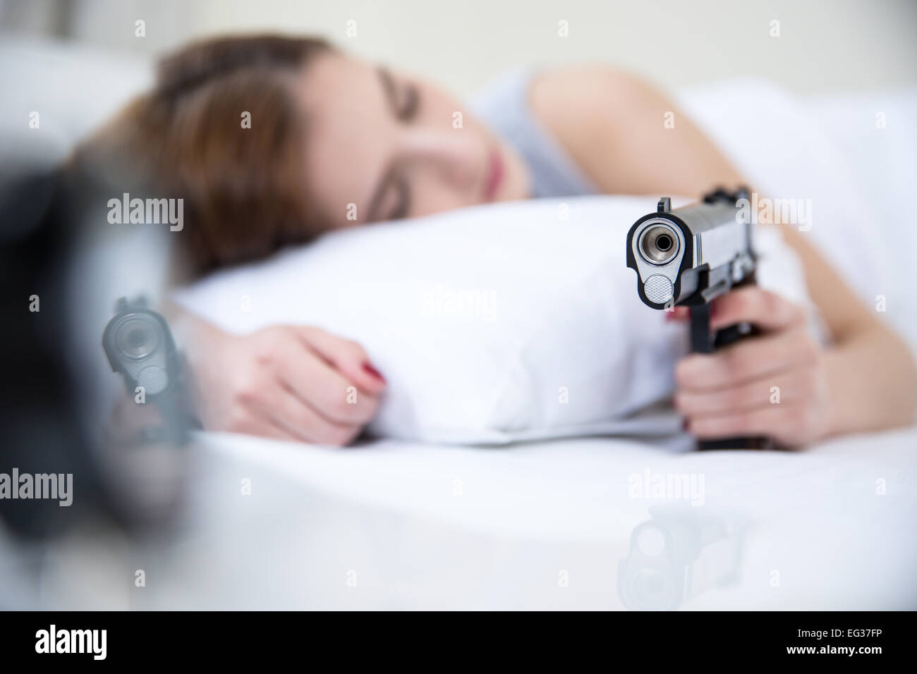 Woman in bed sleeps with hand on gun weapon home security. Focus on gun Stock Photo