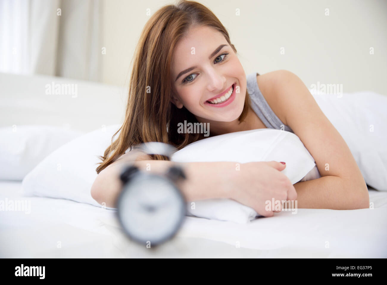 Pretty happy girl waking up in the morning and looking on alarm clock Stock Photo