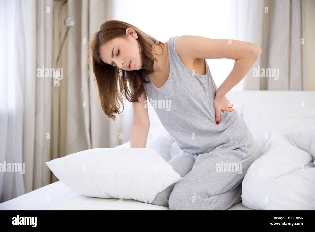 Young woman sitting on the bed with back pain Stock Photo