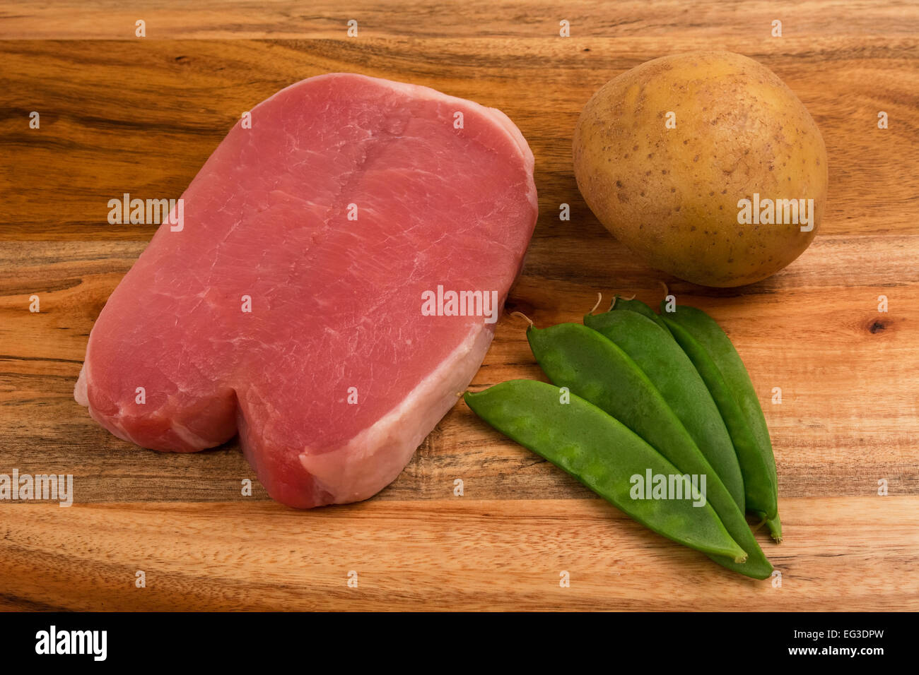 pork chop uncooked on a chopping board with peas and a whole uncooked potato medium closeup studio shot Stock Photo