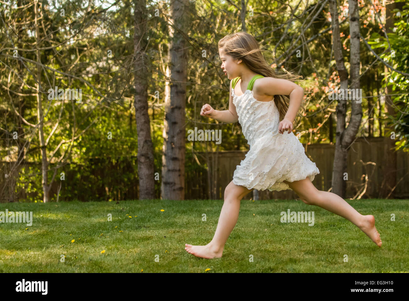 Seven year old girl wearing a sleeveless dress, running barefoot in her backyard in Issaquah, Washington, USA Stock Photo