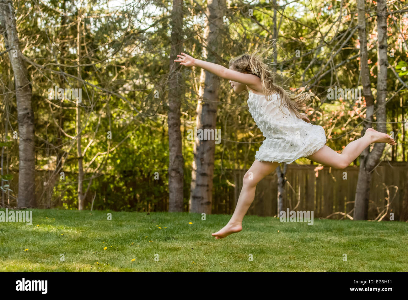 Seven year old girl running and leaping barefoot with great energy and excitement in her backyard in Issaquah, Washington, USA Stock Photo
