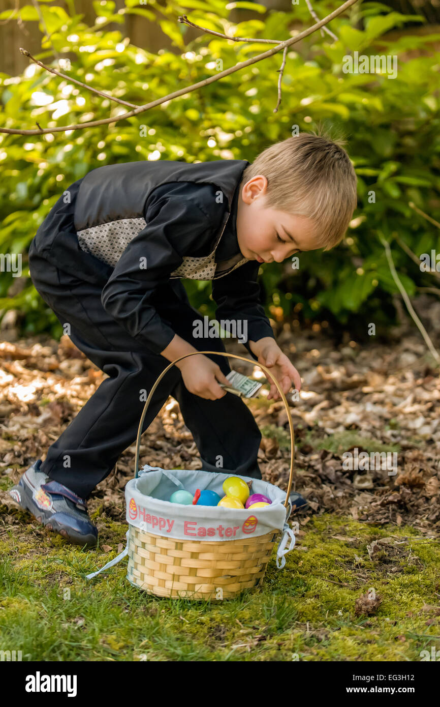 Four year old boy searching for Easter eggs in his backyard, and amazed to find a dollar bill in one of them Stock Photo