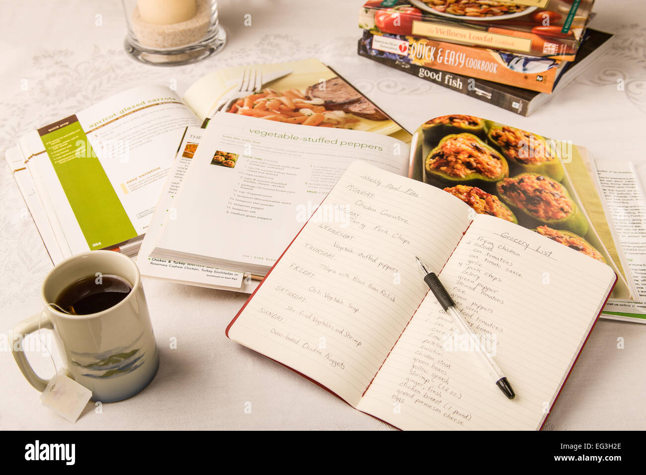 Meal planning at the dining room table, with healthy cookbooks spread open.  A notepad shows dinner meals and groceries by day. Stock Photo