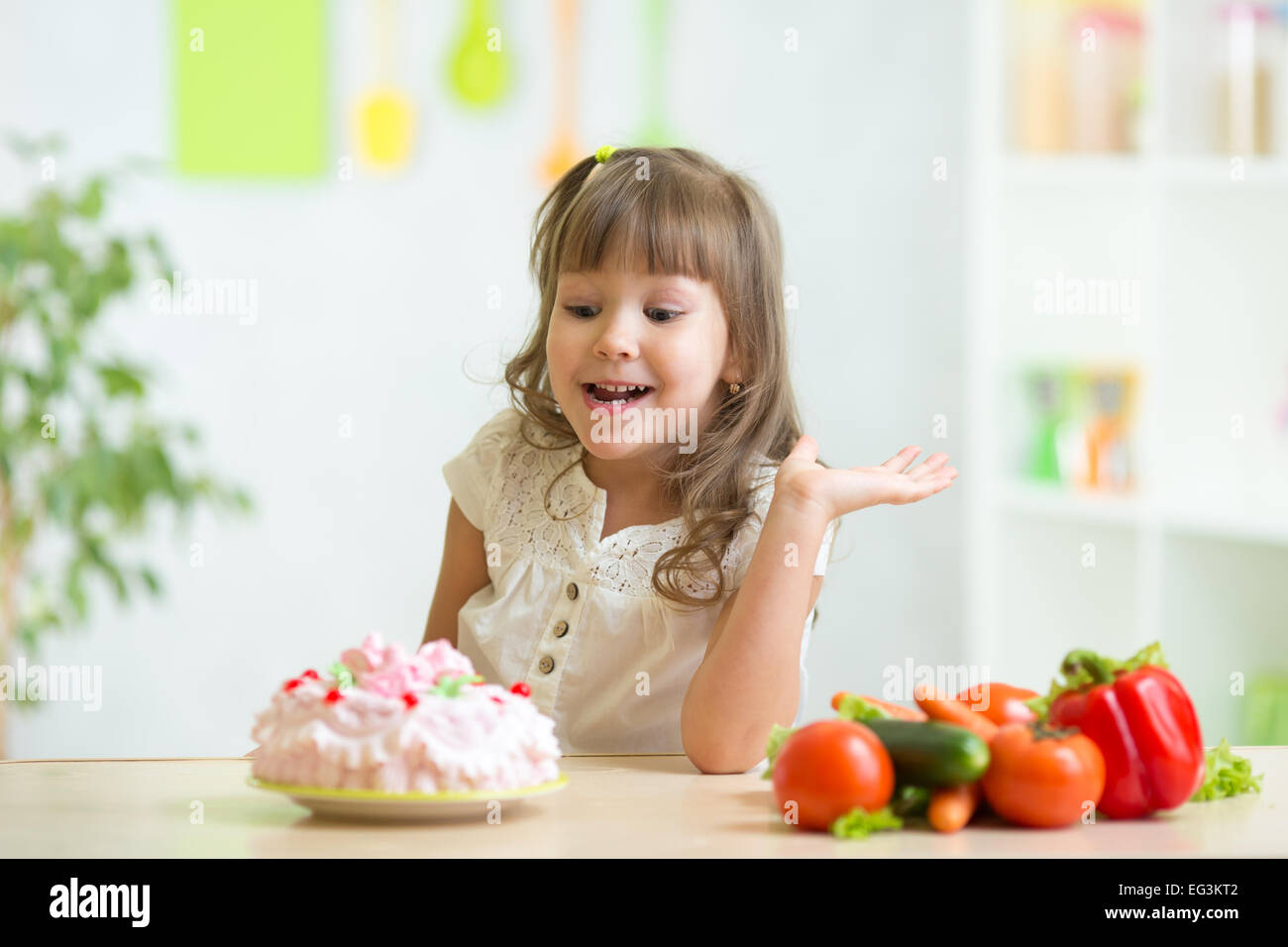 kid choosing between healthy vegetables and tasty cake Stock Photo