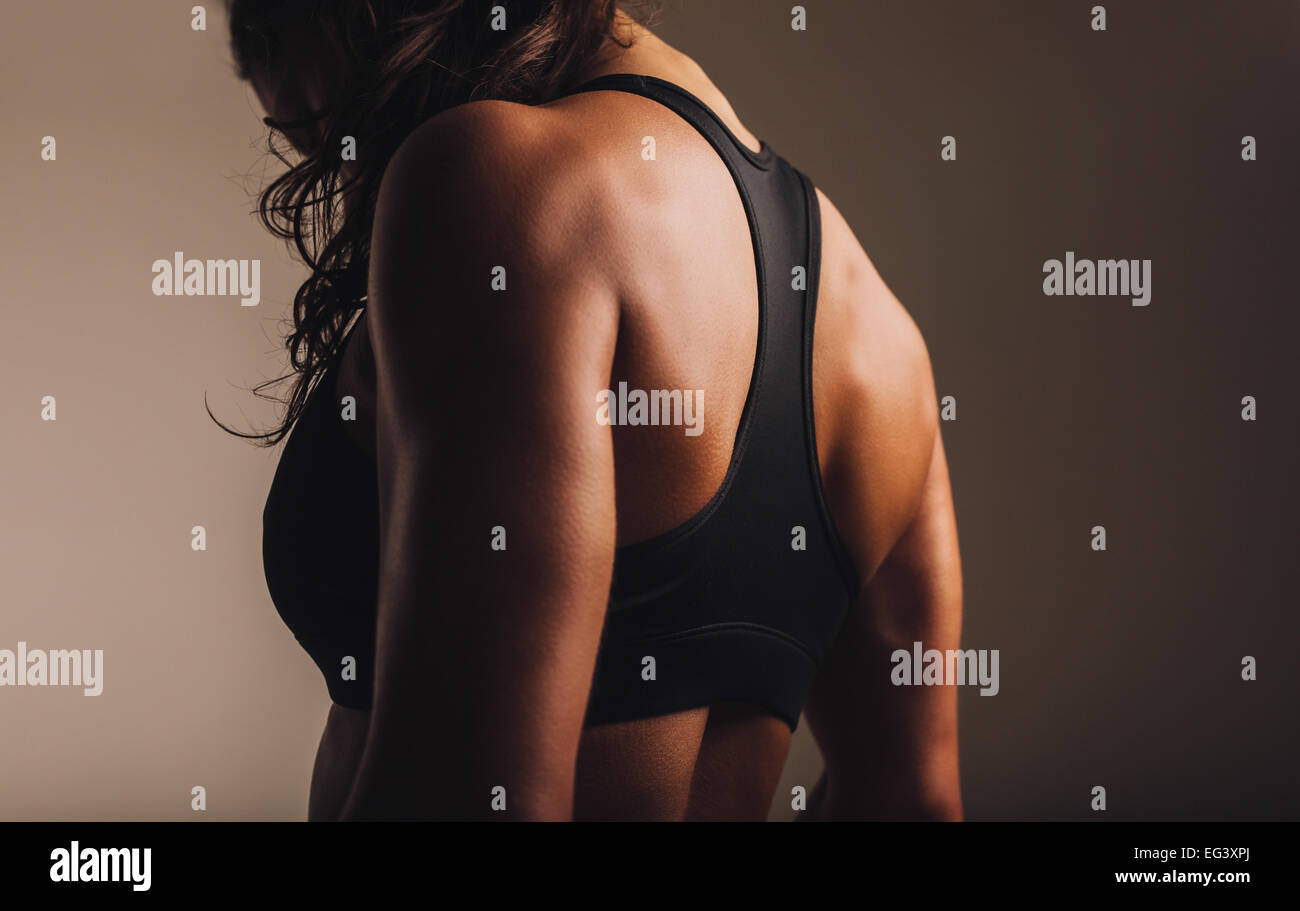 Fit and muscular woman in sports bra standing with her back towards camera. Rear view of fitness female with muscular body. Stock Photo