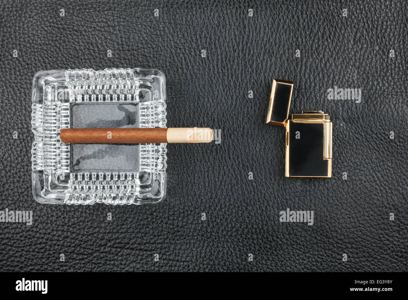 Lighter and glass ashtray with cigar, lying on genuine black leather Stock Photo