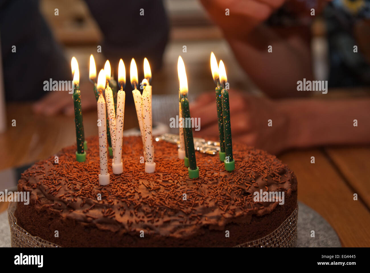 thirteen burning candles on a homemade chocolate birthday sponge cake covered in chocolate and candy sprinkles Stock Photo