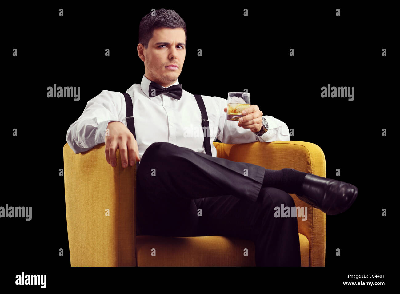 Serious man sitting in an armchair and drinking whiskey on black background Stock Photo