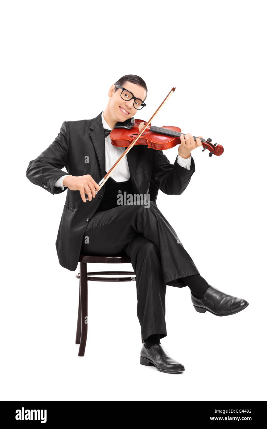 Vertical shot of a young violinist playing a violin seated on a chair isolated on white background Stock Photo