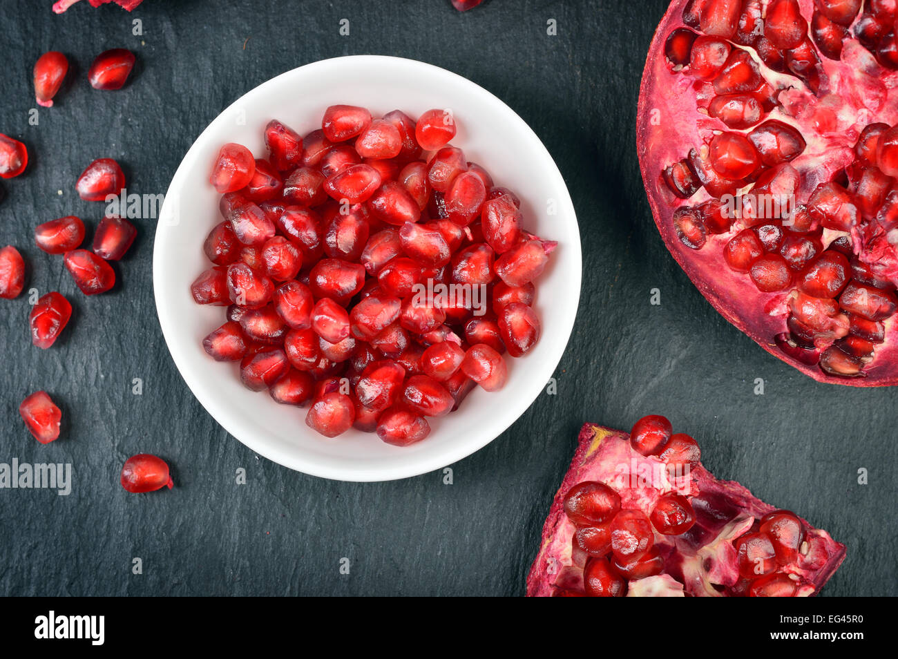 Red pomegranate seeds in a white bowl on table. Open fresh ripe pomegranate. Stock Photo