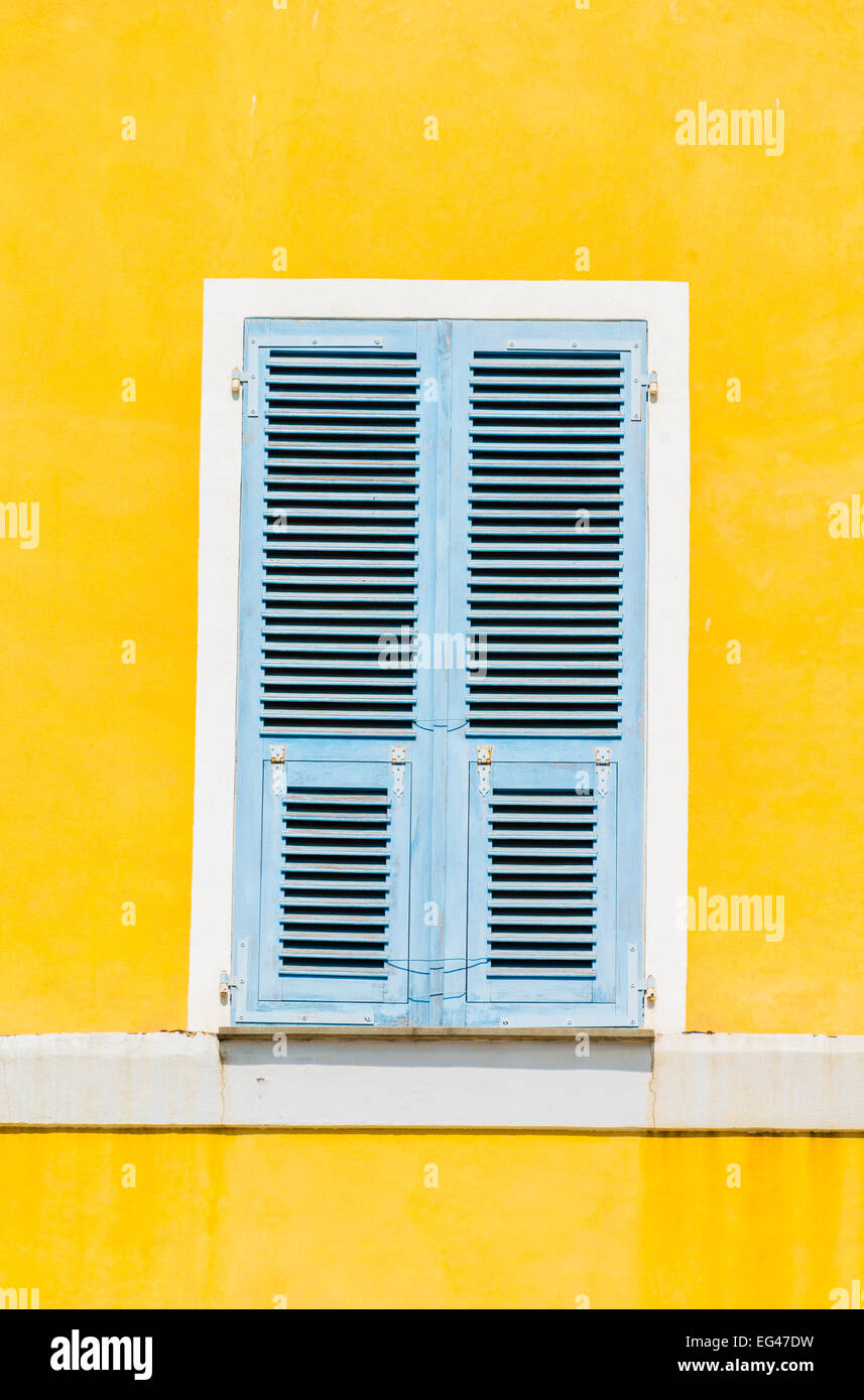 Yellow plastered wall with closed bright blue wooden shutters, Corsica, France Stock Photo
