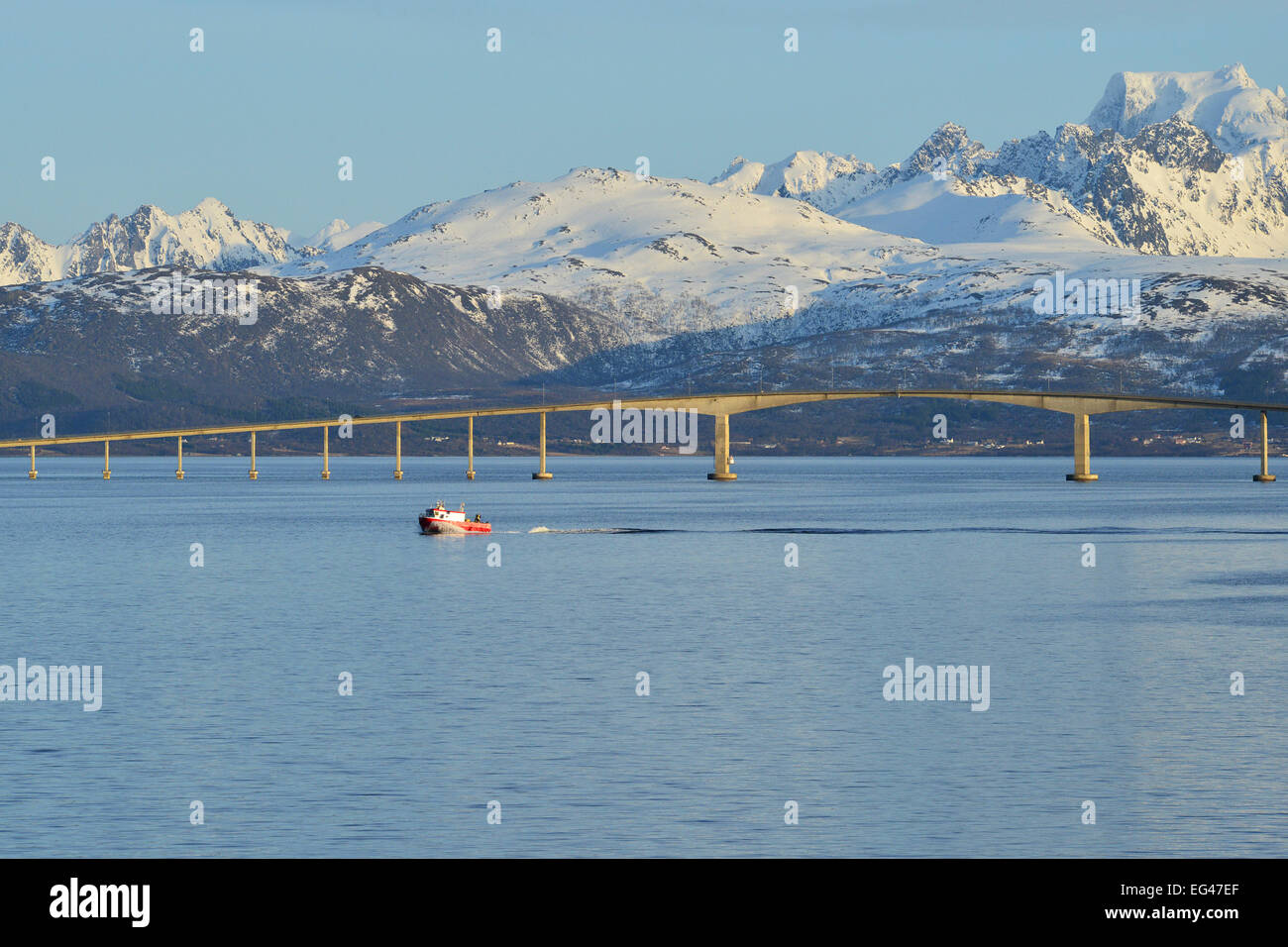Red boat in front of HadseRM Bridge across the strait, at the back the snow-capped mountains of Hinnøya isRMand, RMangøysund Stock Photo