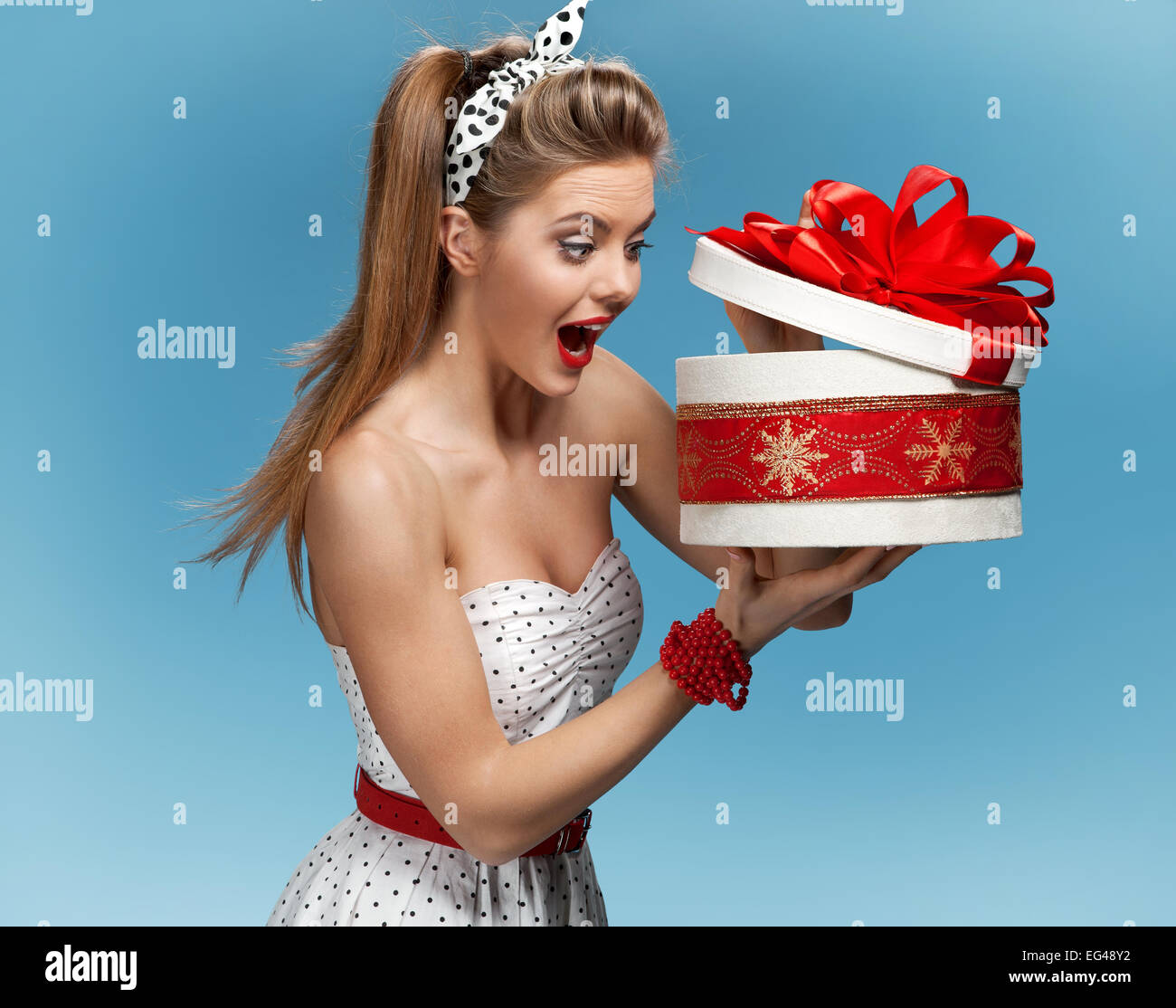 Portrait of happy woman opening gift box against blue background. Holidays, holiday, celebration, birthday and happiness concept Stock Photo