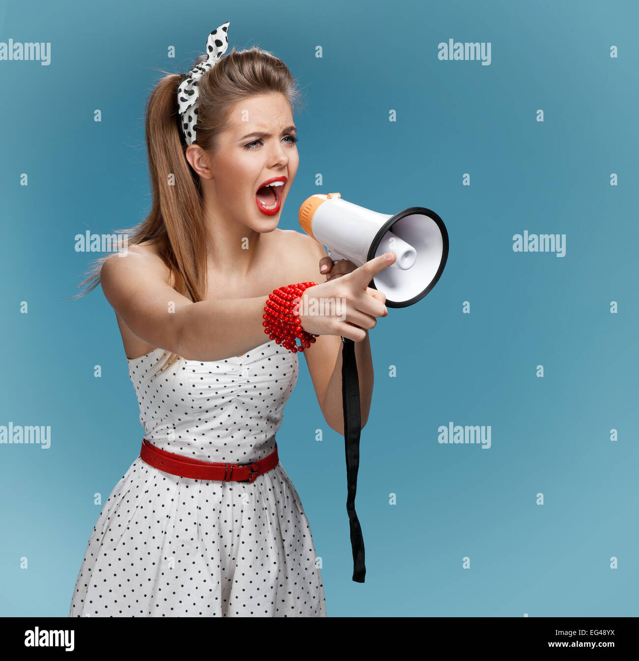Angry pin-up girl shouting into a megaphone, mouthpiece, speaking trumpet. Filmmaking or film production concept Stock Photo