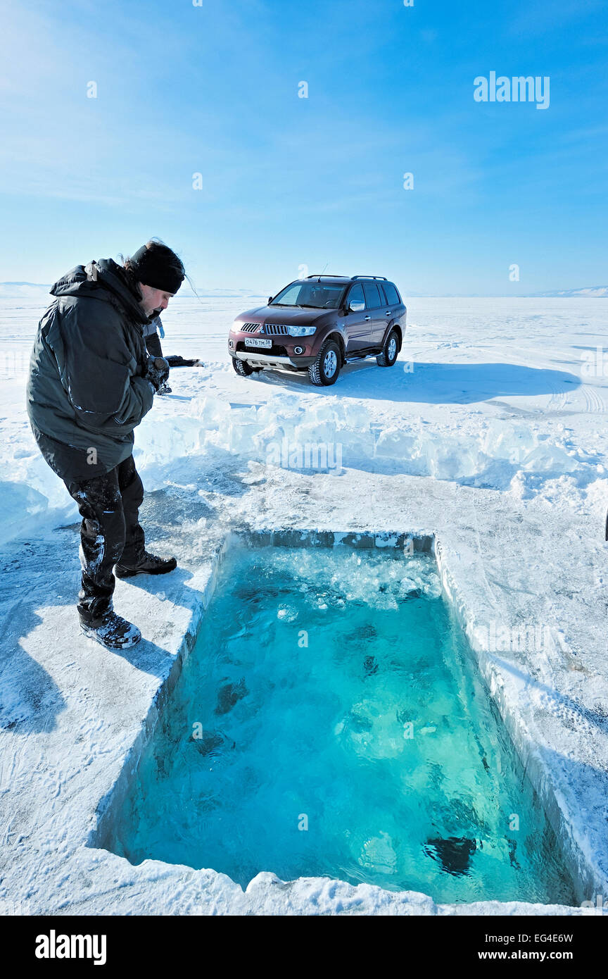 Man looking into ice hole dug ice diving Lake Baikal Siberia Russia