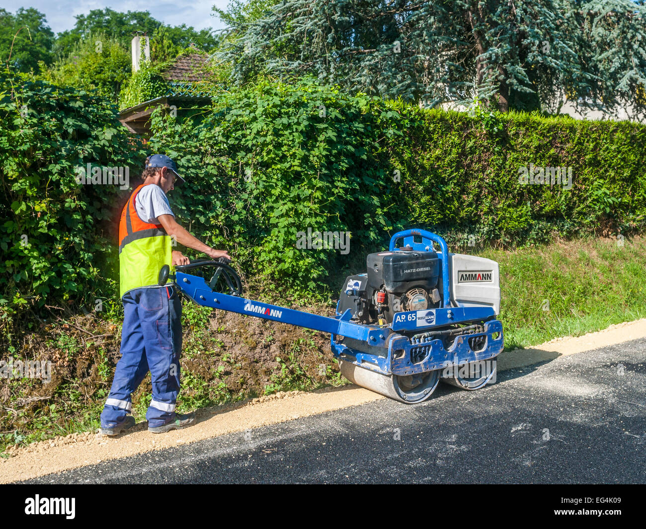 Worker and machine for tamping down edge of road works - France. Stock Photo