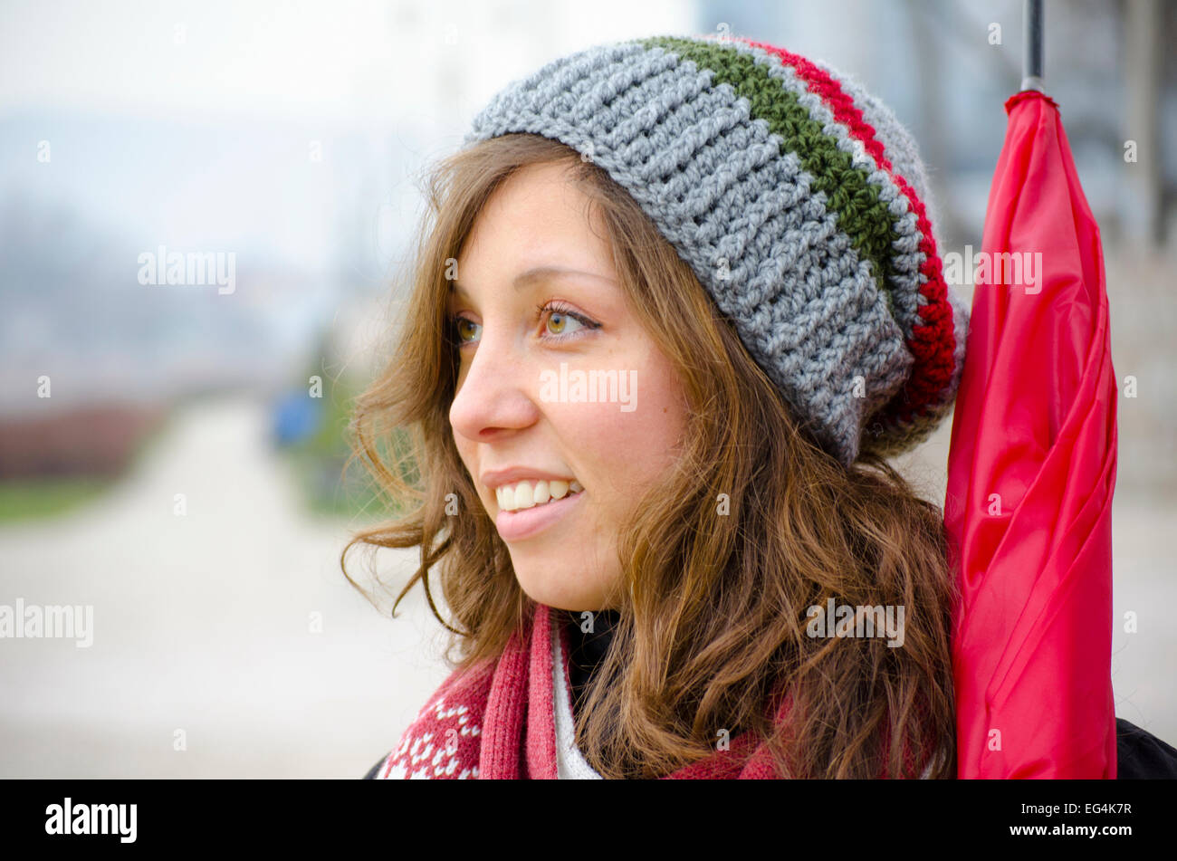 Young brunette wearing a hand made woolen hat and a red umbrella outdoors Stock Photo