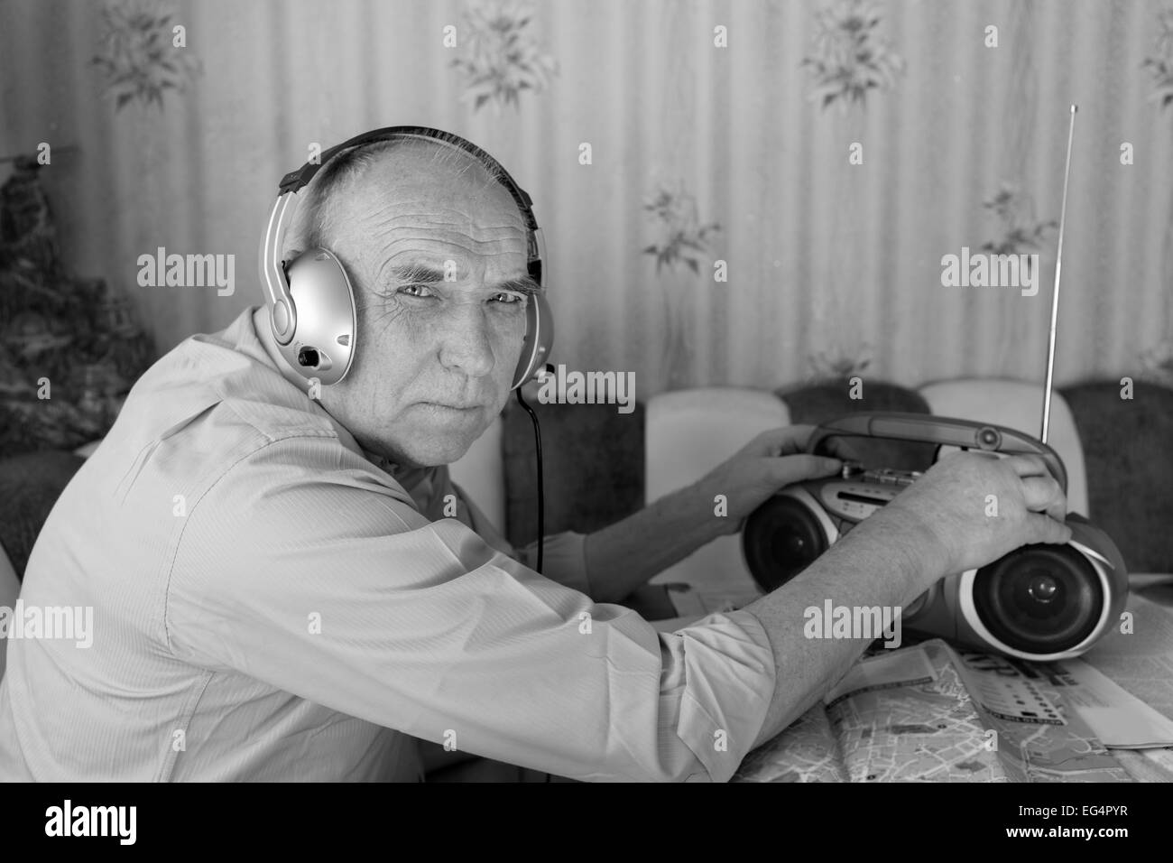 Close up Old Man Listening Music from Radio with Headset While Looking at the Camera. Captured in Monochrome Stock Photo