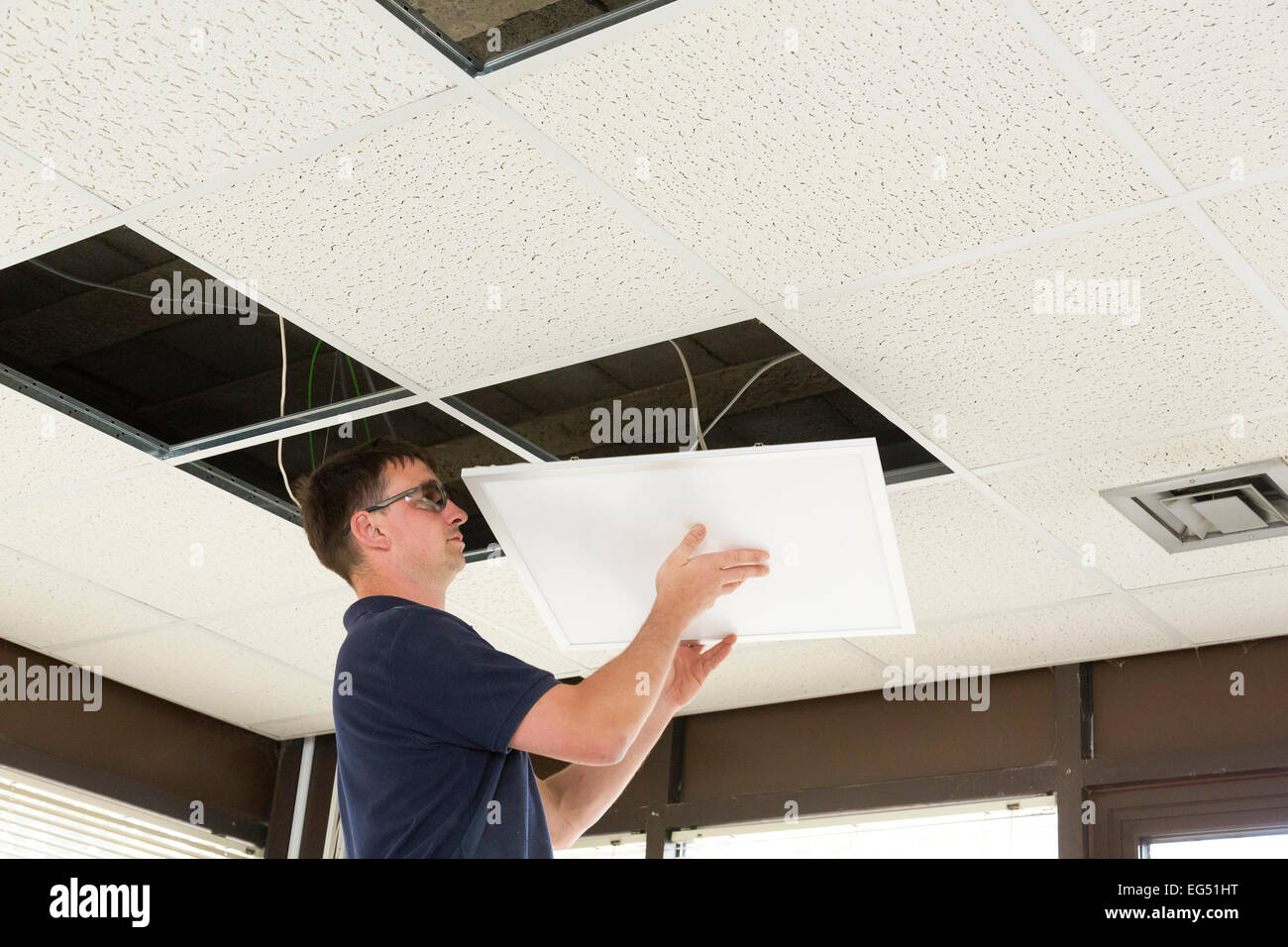 electrician installing LED flat panel lighting in a suspended ceiling Stock Photo