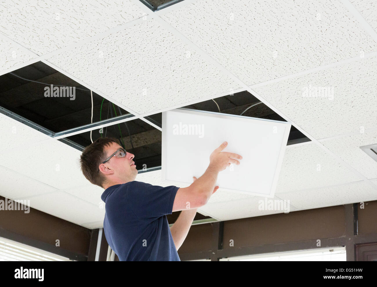 electrician installing LED flat panel lighting in a suspended ceiling Stock Photo