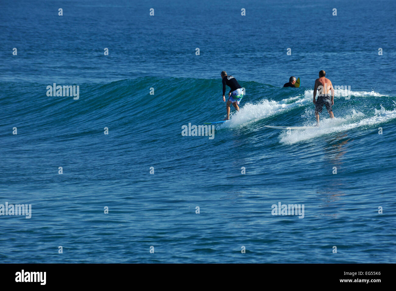 Two active senior male surfers enjoy riding surfboards down gentle wave in bay of Durban, KwaZulu-Natal, South Africa Stock Photo