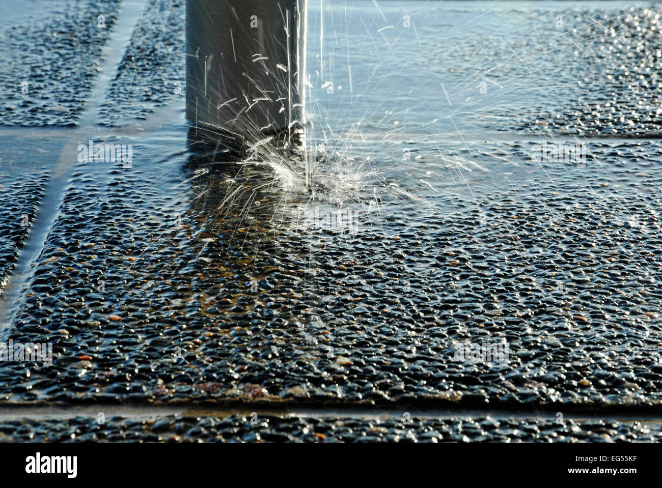 Water from leaking tap falling on paving in splash of flying droplets Stock Photo