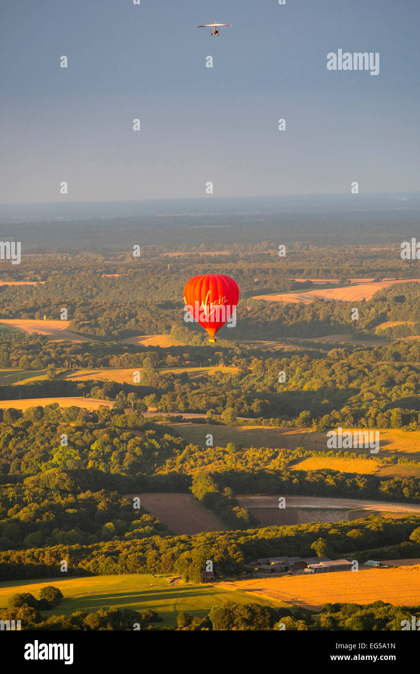 Red hot air balloon and hang glider flying over rural landscape, South Oxfordshire, England Stock Photo