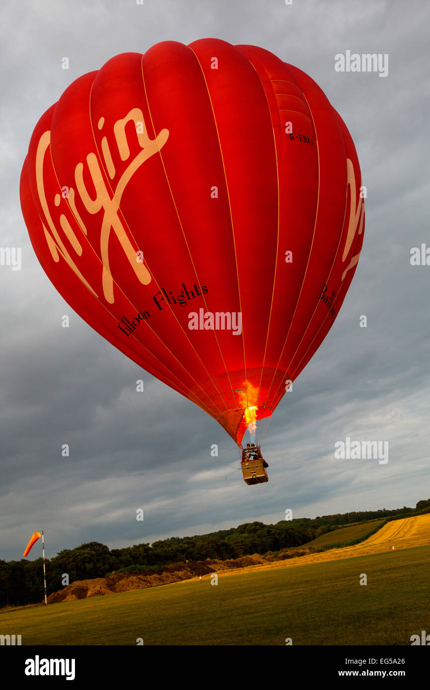 Hot air balloon floating above field using gas burner, South Oxfordshire, England Stock Photo