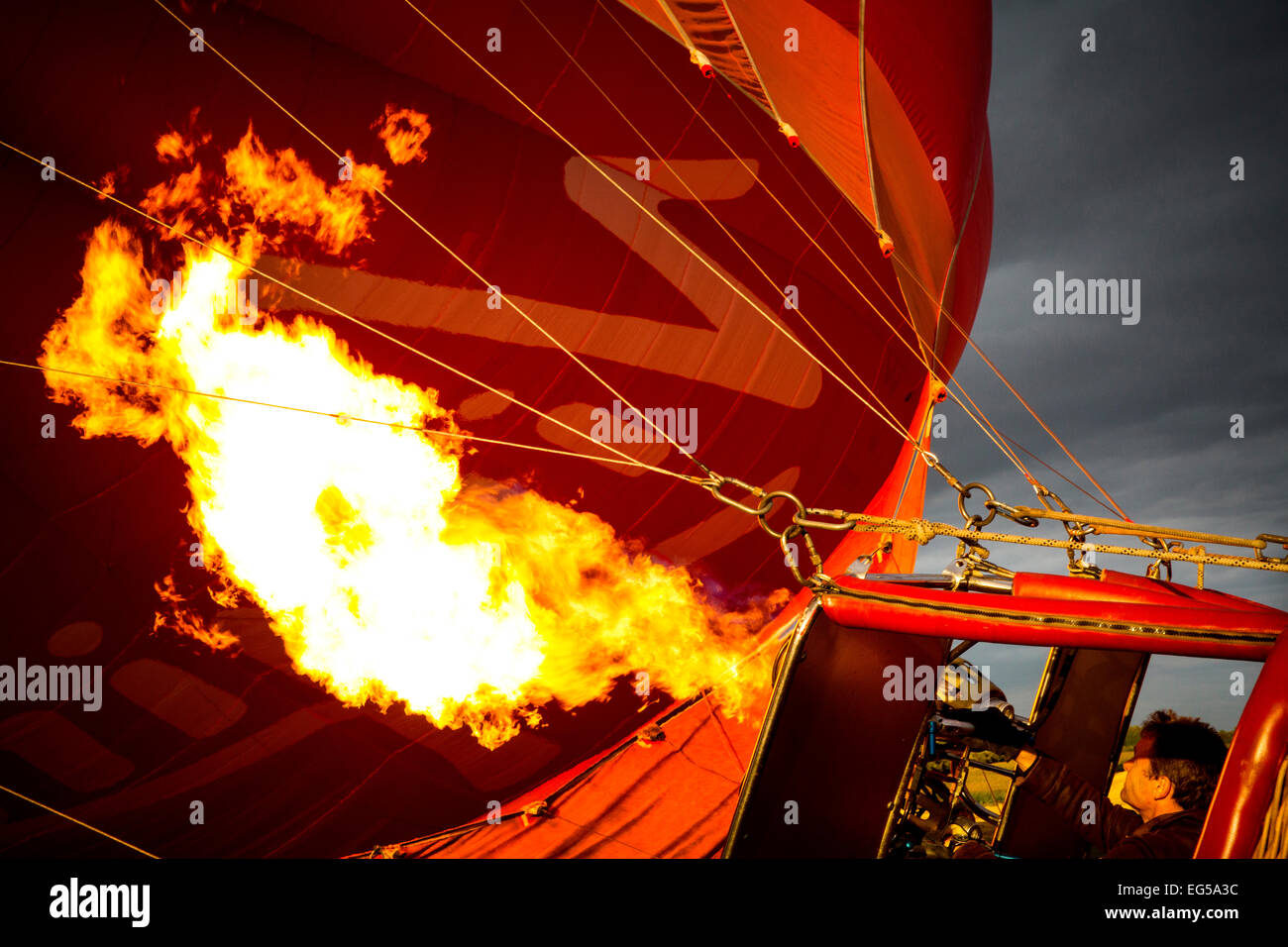 Man controlling gas burner flames inflating red hot air balloon, South Oxfordshire, England